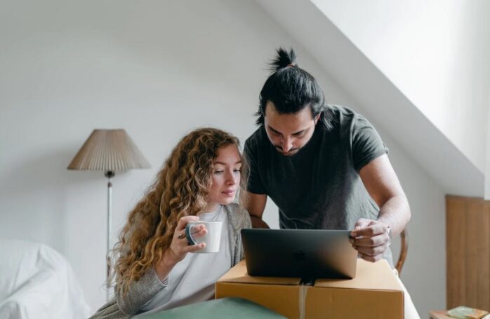 a young couple browsing laptop on cardboard box