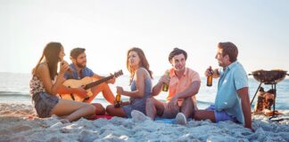 A group of friends celebrating on a beach with music, drinks and BBQ