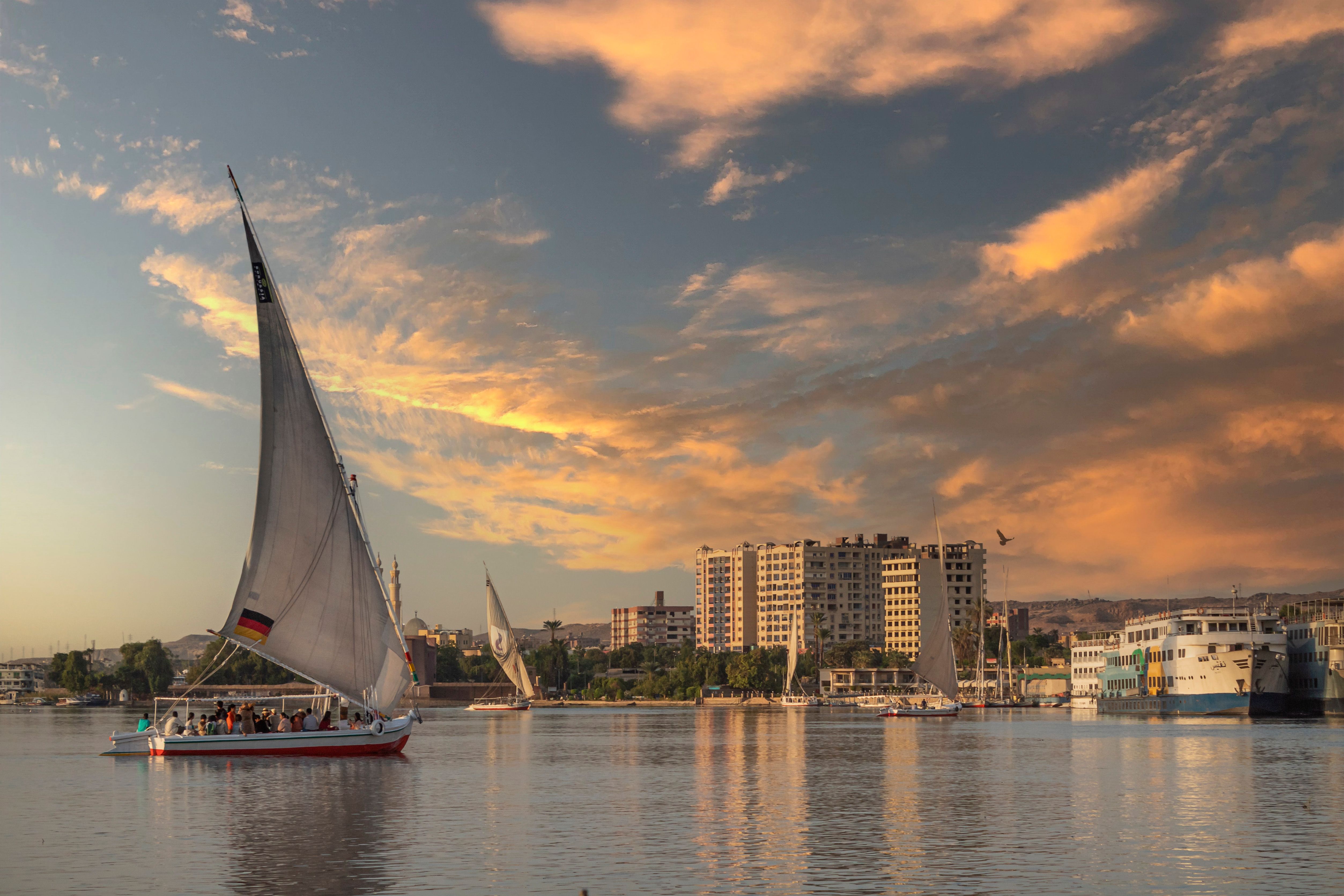 A traditional felucca sails the Nile at sunset with cityscape in the background